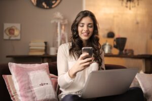 using social media Photo by Andrea Piacquadio: https://www.pexels.com/photo/woman-sitting-on-sofa-while-looking-at-phone-with-laptop-on-lap-920382/
